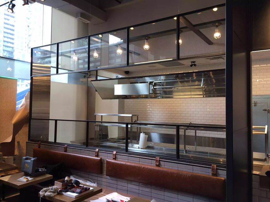 Custom multi-panel steel-framed glass partition wall separating an open kitchen from the dining area.