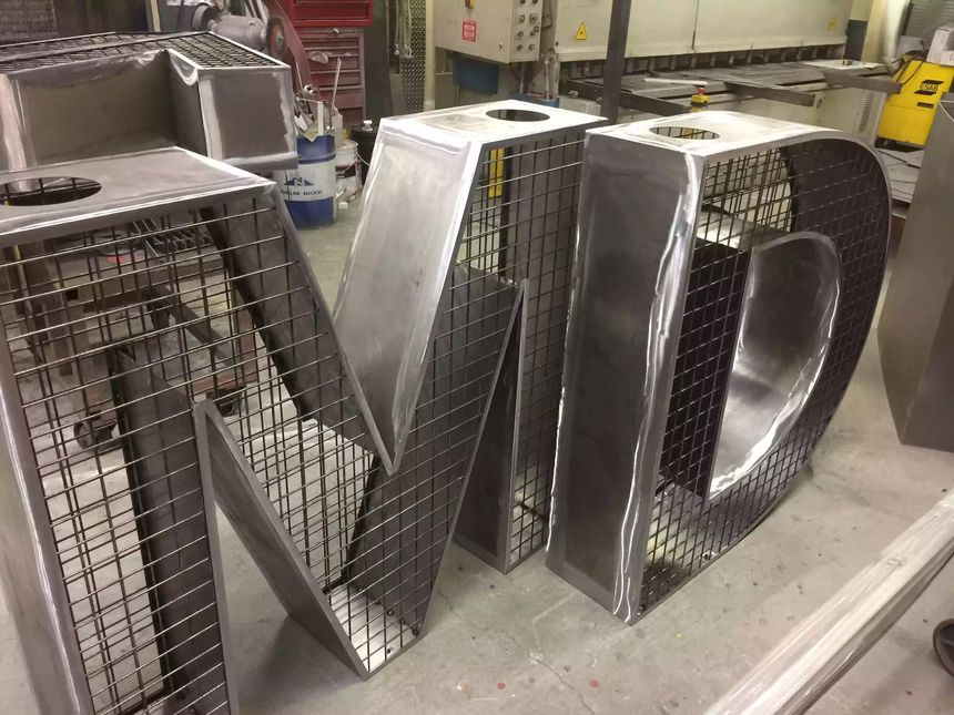 Oversized custom steel channel letters fabricated in-shop, combining solid steel faces with welded mesh side panels.