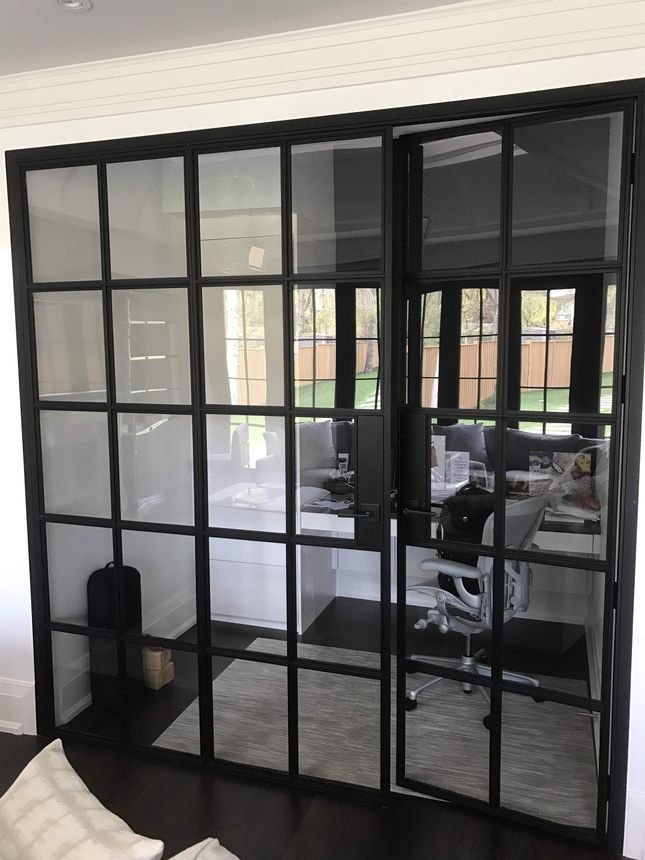 Floor-to-ceiling black steel grid partition with clear and frosted glass panels and an integrated steel-framed door.