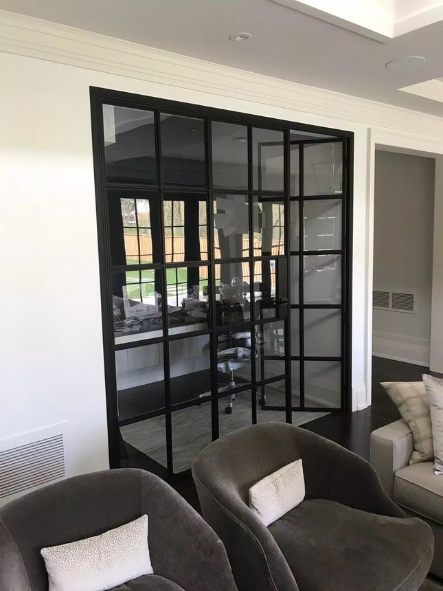 Custom black steel-framed glass partition with classic grid divisions, dividing an interior home office from the living room.