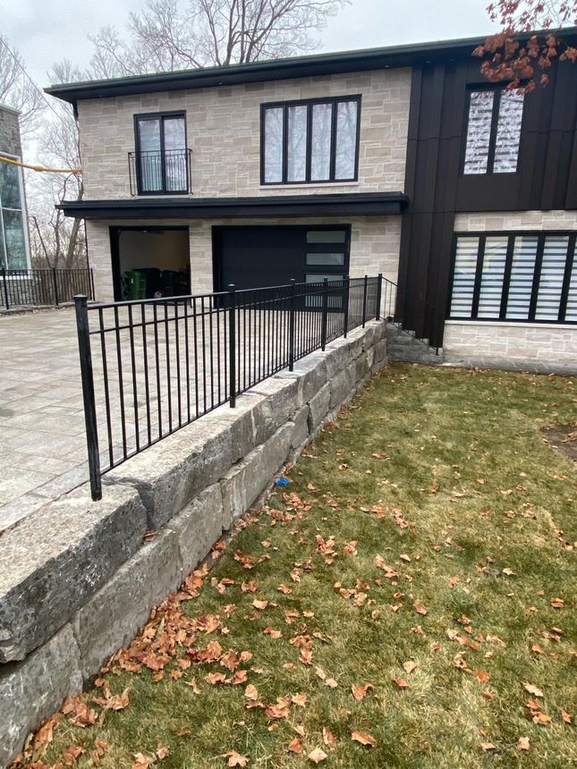 Black powder-coated metal picket fence mounted on a stone retaining wall