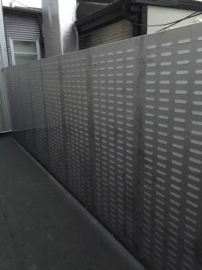 A run of custom perforated steel privacy fence panels with a patterned cut design, providing screening and airflow in a powder-coated dark finish.