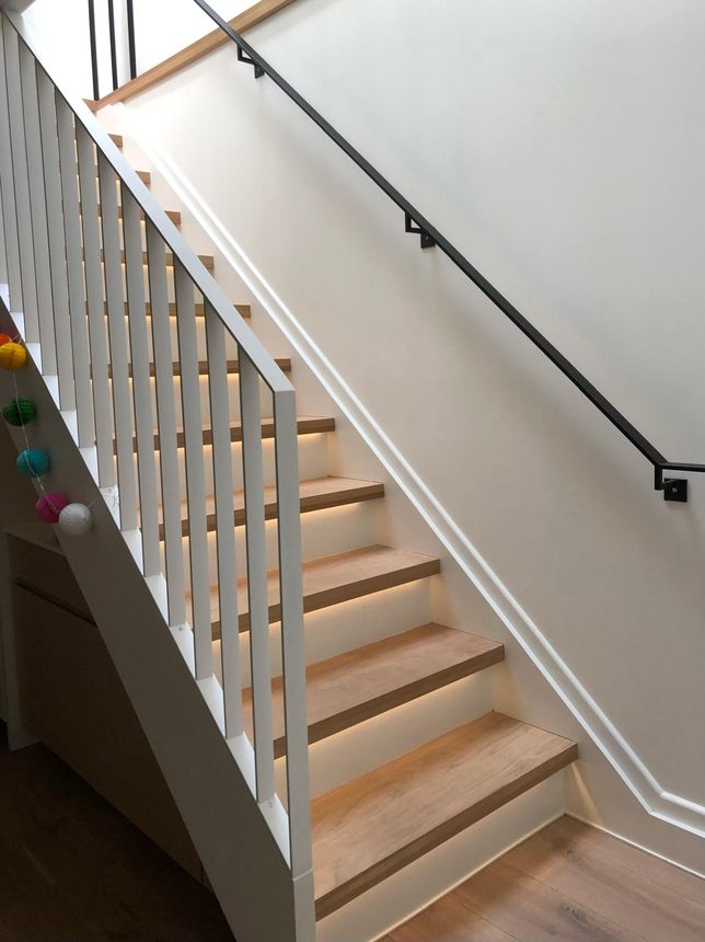 Modern interior staircase featuring slim white steel balusters and a sleek black wall-mounted handrail