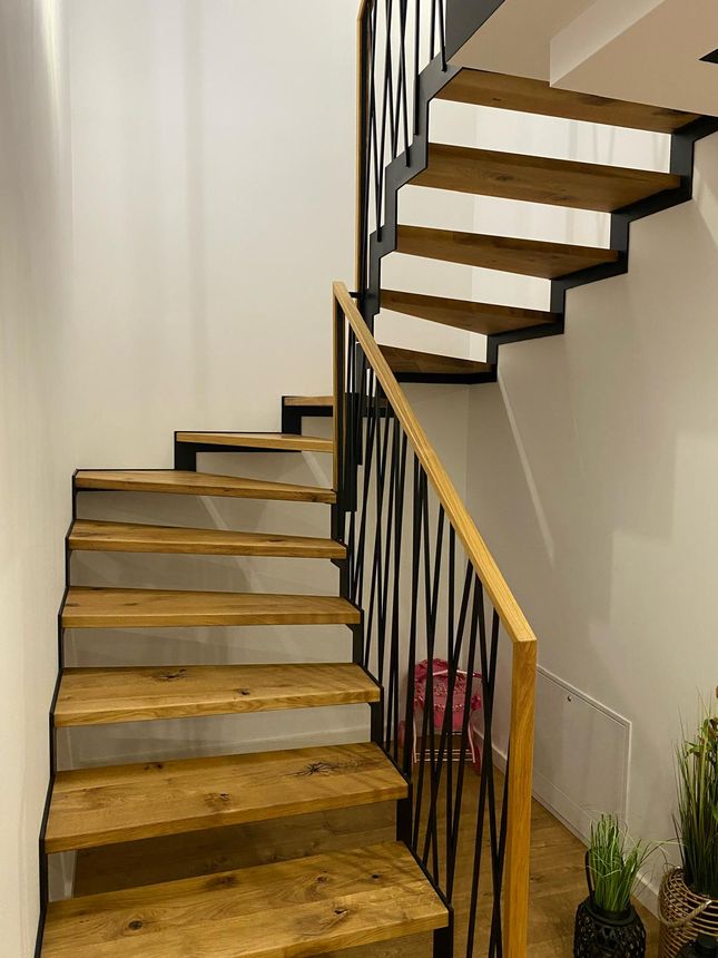 Modern open-riser staircase with a custom geometric iron railing and wood-capped handrail