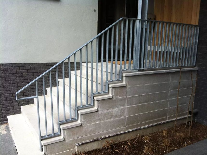 Galvanized steel exterior staircase railing with vertical pickets, finished entrance installation.