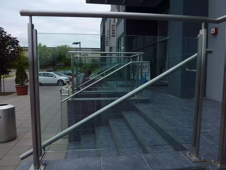 Stainless steel and glass guardrail system lining an accessible entrance ramp and stairs at a commercial storefront, combining safety with a clean modern look.